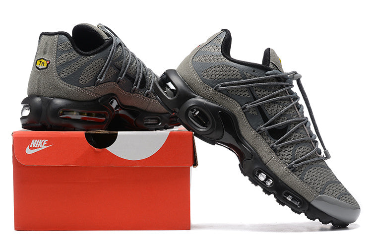 Pair of grey and black Nike Air Max Plus sneakers displayed on a red shoe box.