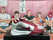Side profile of a grey and burgundy Nike basketball sneaker with a visible Swoosh, patterned heel panel, and white midsole.