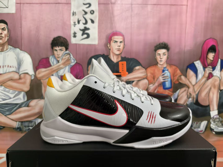 Pair of white and black Nike basketball sneakers displayed on a black shoebox, showing red-edged side branding and yellow heel accents.
