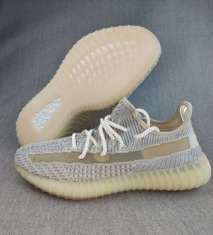 Side view of gray and cream Yeezy 350 V2 sneakers showing the knit upper, side stripe, laces, and translucent ribbed sole.