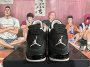 Rear view of black and grey high-top sneakers with white Jumpman heel logos and speckled midsoles on a shoebox.