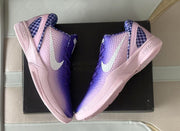 Top-down view of the pair positioned over a black box, showing violet uppers, light-colored Swooshes, and pink midsoles.