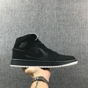 Side profile of a black Air Jordan 1 Mid sneaker with a white outsole and speckled black overlays.