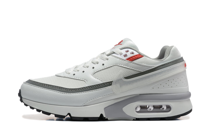 Side view of a white Nike sneaker with grey trim, red accents, a translucent Swoosh, and a visible heel air unit.