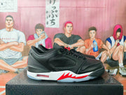 Side view of a black sneaker showing perforated panels, a white midsole, red jagged accent details, and a translucent outsole section.