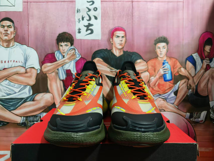 Pair of black, yellow, orange, and green basketball sneakers shown from the front on a shoebox.