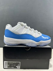 Side view of white and blue Jordan Air Jordan 11 Retro Low sneakers displayed on a black shoe box; the box label shows EU 42 and style code FV5104 100.