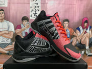 Angled view of paired Nike basketball sneakers showing the black and pink upper, white side graphics, orange laces, and translucent soles.