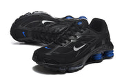 Angled view of black Nike Shox R4 sneakers with silver Swooshes and blue details.
