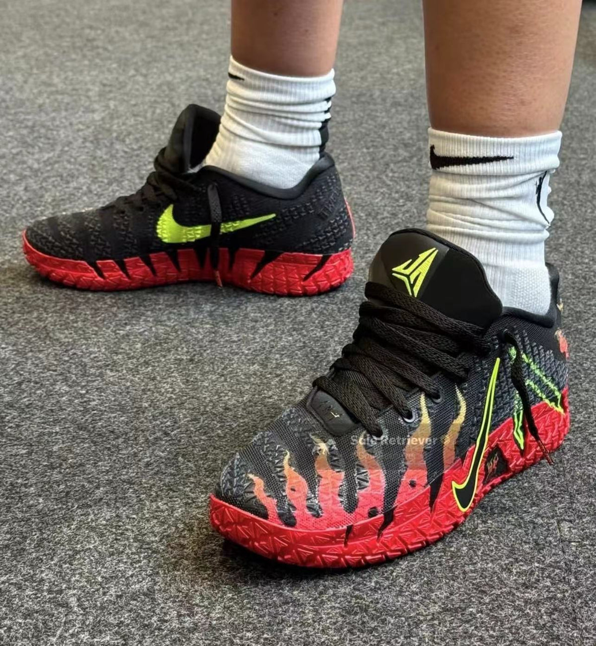 Black Nike basketball sneakers with neon green branding, graphic detailing, and bright red textured midsoles shown on a model.