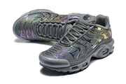 Angled view of dark grey Nike Air Max Plus sneakers with multicolor iridescent overlays