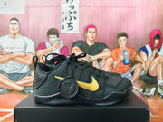 Side view of a black basketball shoe with gold side detailing and a circular Kobe logo accessory.