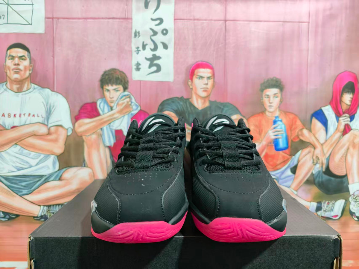 Front view of black and grey Jordan basketball sneakers with bright red-pink outsoles on a shoebox.