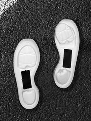 White shoe soles showing molded cushioning areas and black rectangular inserts on a dark textured surface.