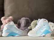Pair of white and blue Nike HD2008 kids high-top sneakers displayed against soft toys.