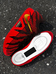 Close-up of a brown and red sneaker with gold Swoosh branding beside its exposed white sole structure.