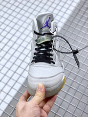 Front view showing the grey toe box, black laces, translucent lace accessory, and purple tongue branding.