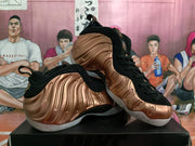 Angled view of a pair of rose-gold and black Nike sneakers displaying the sculpted side panels, black uppers, and contrasting outsoles.