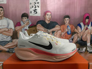 Side view of a white Nike sneaker showing the black Swoosh, pink-red midsole accent, and layered sole.