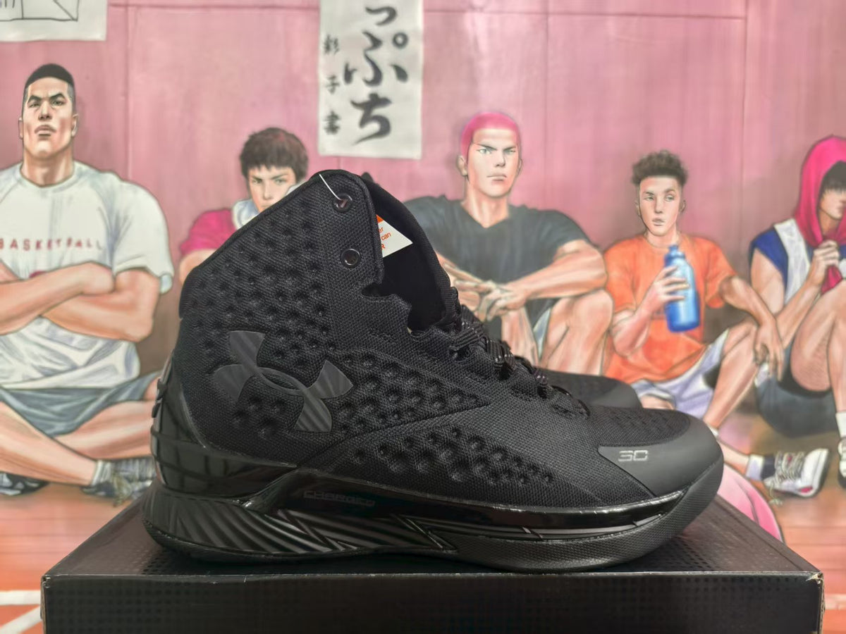 Side view of black and gray Under Armour high-top basketball sneakers displayed on a shoebox.