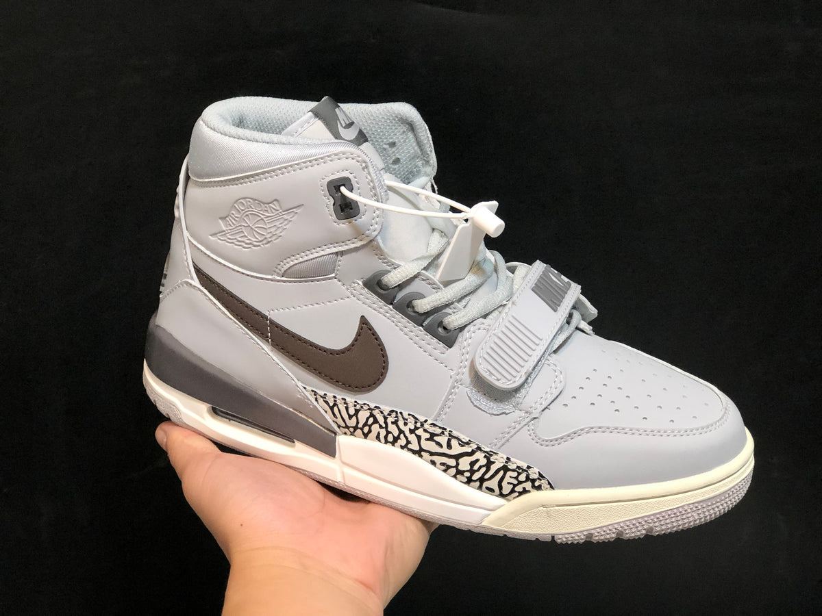 Side-front view of a grey and white Air Jordan Legacy 312 high-top sneaker with a brown Swoosh, elephant-print side panel and midfoot strap.
