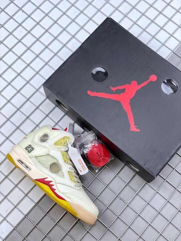 Off-white Air Jordan 5 sneaker beside a black Jordan shoebox, with red and black accessories visible.