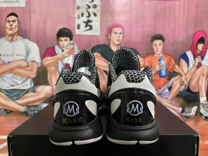 Rear view of black and white basketball sneakers showing Kobe and Gigi heel graphics, a stylized M emblem, and the number 2 theme.