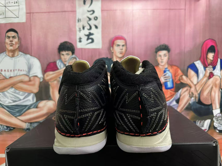 Rear view of black high-top basketball sneakers with geometric stitching, red accents, and cream-colored soles.