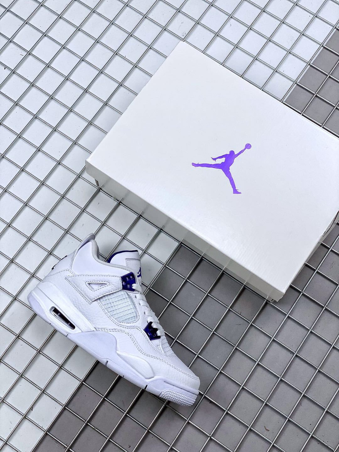 White and purple Air Jordan 4 sneaker beside a white Jordan shoebox.