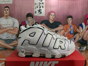 Side view of a white sneaker with layered AIR lettering, black outlines, perforated panels and a visible sole window.