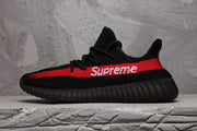 Side profile of the black sneaker with a red stripe, white Supreme lettering, and ribbed outsole.