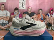 Side view of a Brooks light gray-white running shoe showing the dark logo, pink midsole accents, and DNA TUNED marking