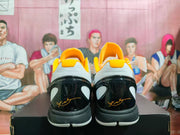 Rear view of the white and black basketball shoes, showing glossy black heels and yellow-orange collar accents.