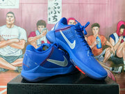 Angled product view showing one blue basketball sneaker resting over the matching shoe, with white side logos and red accents.