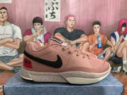 Side view of a pink sneaker with black side branding, a speckled off-white midsole, and red heel graphics.
