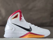 Side view of a white high-top Nike basketball shoe with black Swoosh, red collar trim, and gold-toned midsole accent.