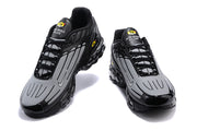 Front view of a pair of black and grey Nike Air Max Plus sneakers.