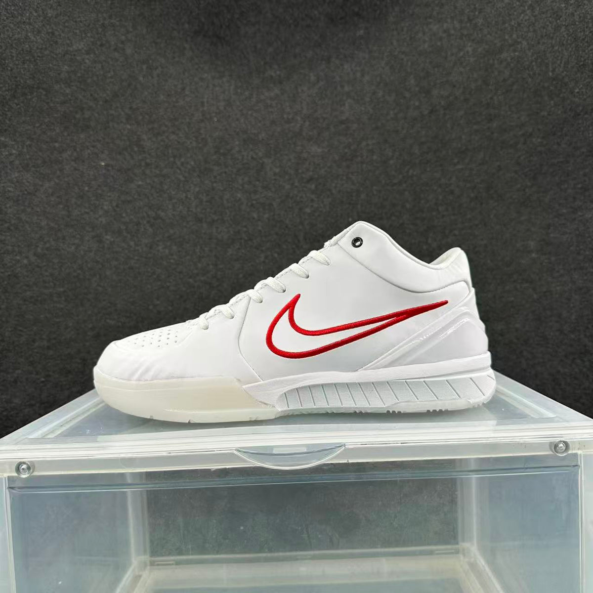 Side view of a white low-top basketball sneaker with red side branding on a clear display box.