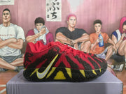 Side view of the red sneaker with black textured overlays, yellow accents, red laces, and a visible swoosh.