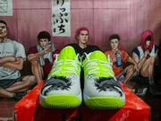 Front view of Nike basketball sneakers showing neon green tongues, white laces, gray toe panels, and black graphic detailing.