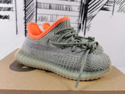 Close side view of a gray knit-style sneaker with orange collar lining, gray laces, and a translucent ribbed sole.