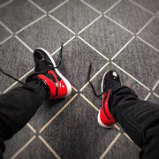 Pair of black and red high-top sneakers being worn, with loose black laces visible.