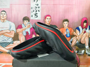 Black slip-on clogs with red trim shown from the side on a box.