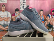 Angled view of a pair of smoke gray low-top sneakers displaying the swoosh panels, pull tabs and light-colored soles.