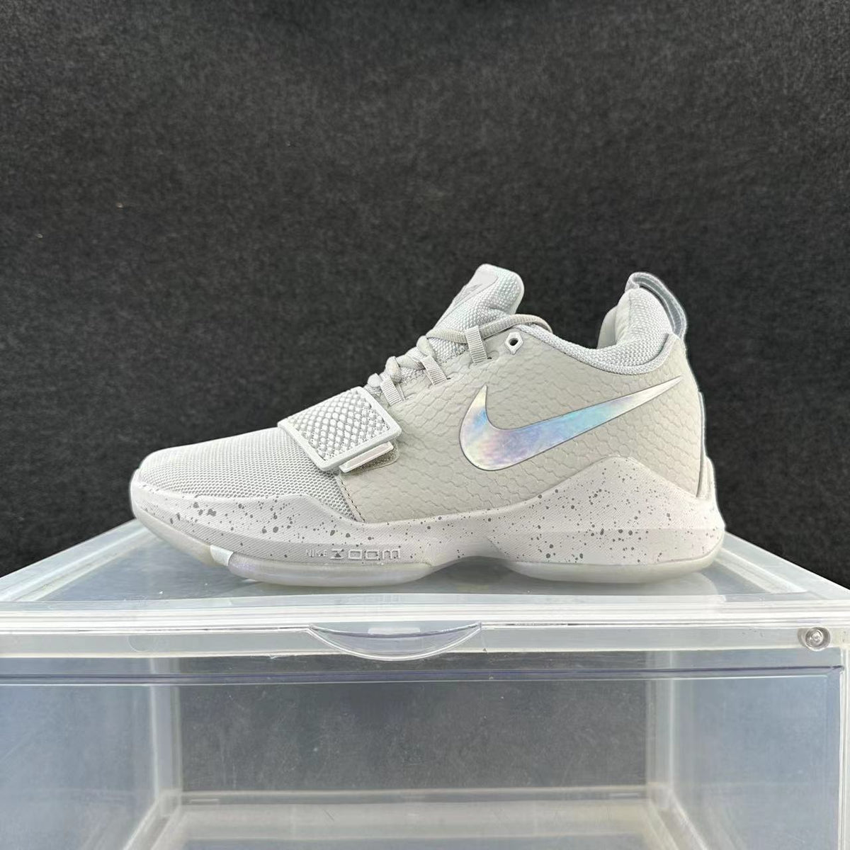 Gray and white Nike basketball shoe with a forefoot strap, iridescent-looking Swoosh, and speckled midsole.