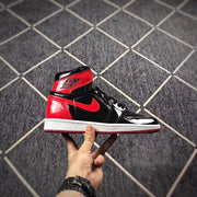 Side profile of a black and red high-top sneaker with a glossy finish and white midsole.