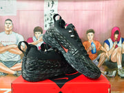 Angled side view showing black Nike shoes, red accents, and sculpted speckled soles.