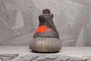 Rear view of the Yeezy 350 V2 sneaker showing the orange stripe, raised heel, and ribbed translucent sole.