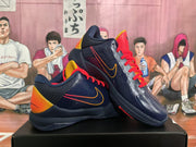Angled view of a pair of dark blue basketball sneakers showing red laces, gold side accents, orange heel panels, and black outsoles.