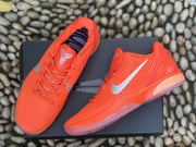 Top and angled view of a pair of orange Kobe 6 sneakers arranged on a black box.